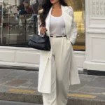 Stylish White Pants Outfits featuring a chic long white coat, wide-leg white pants, and a white top paired with pointed heels and a black handbag.