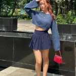 Monochrome Outfits – Young woman in a navy cropped sweater and matching navy pleated mini skirt with white sneakers and a small red handbag, standing outdoors.