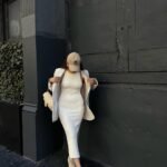 Spring Outfit Ideas in a sleeveless cream ribbed dress, beige oversized jacket, and sneakers, accessorized with a beige NY cap.