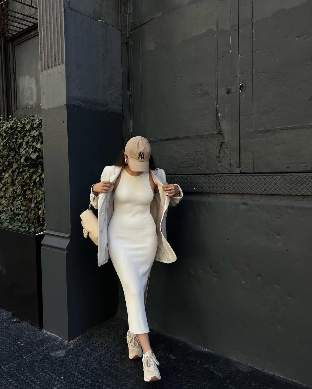 Spring Outfit Ideas in a sleeveless cream ribbed dress, beige oversized jacket, and sneakers, accessorized with a beige NY cap.