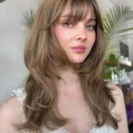 Hairstyles for Medium Length Hair styled with wispy bangs and cascading soft waves, giving a romantic and natural appearance.