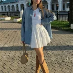 Early Fall Outfit styled with a flowy white mini dress layered under a light denim shirt and finished with tan cowboy boots – perfect for sunny fall afternoons.